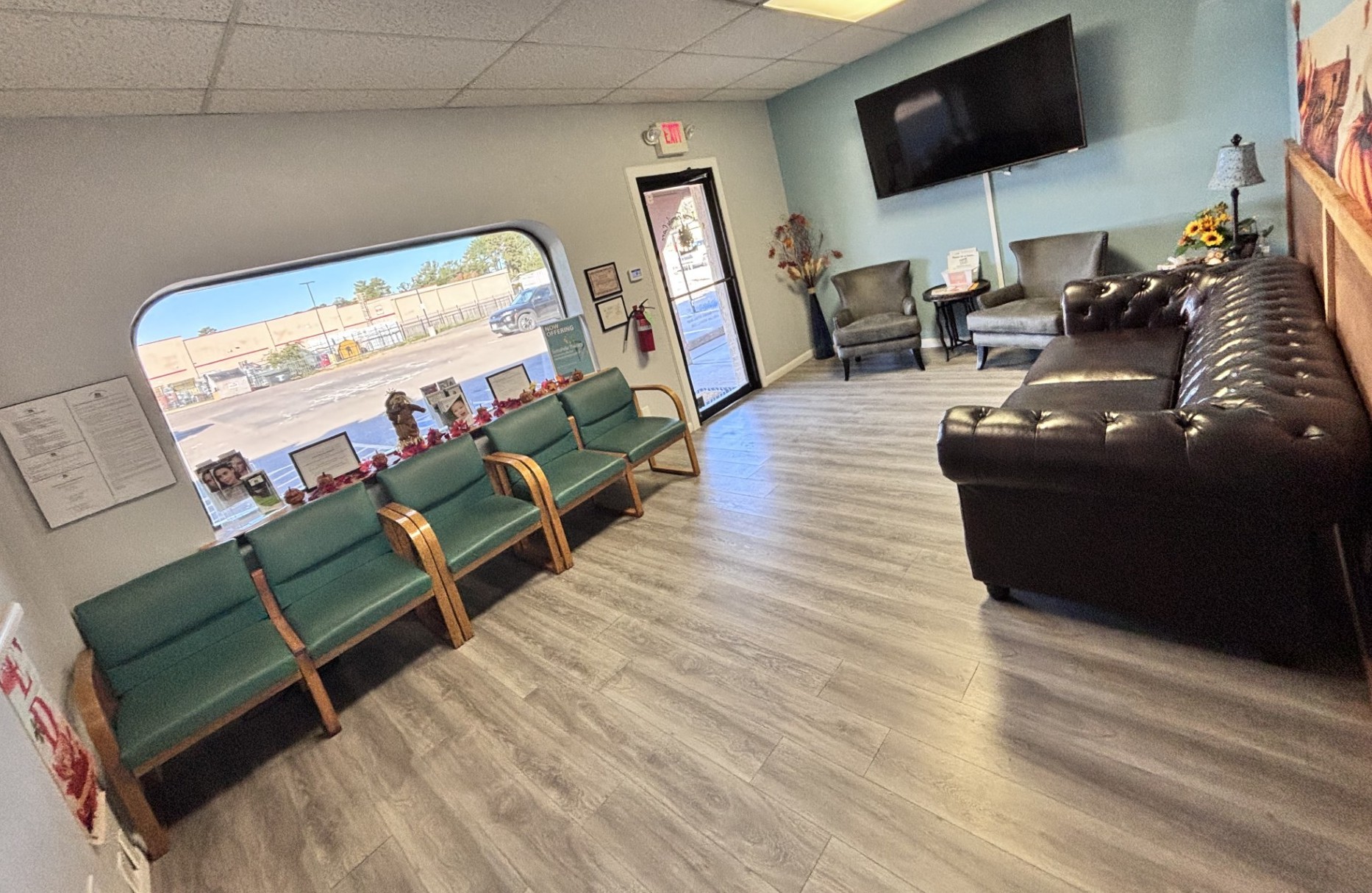 Waiting room with green guest chairs, a black sofa, and a large front window.